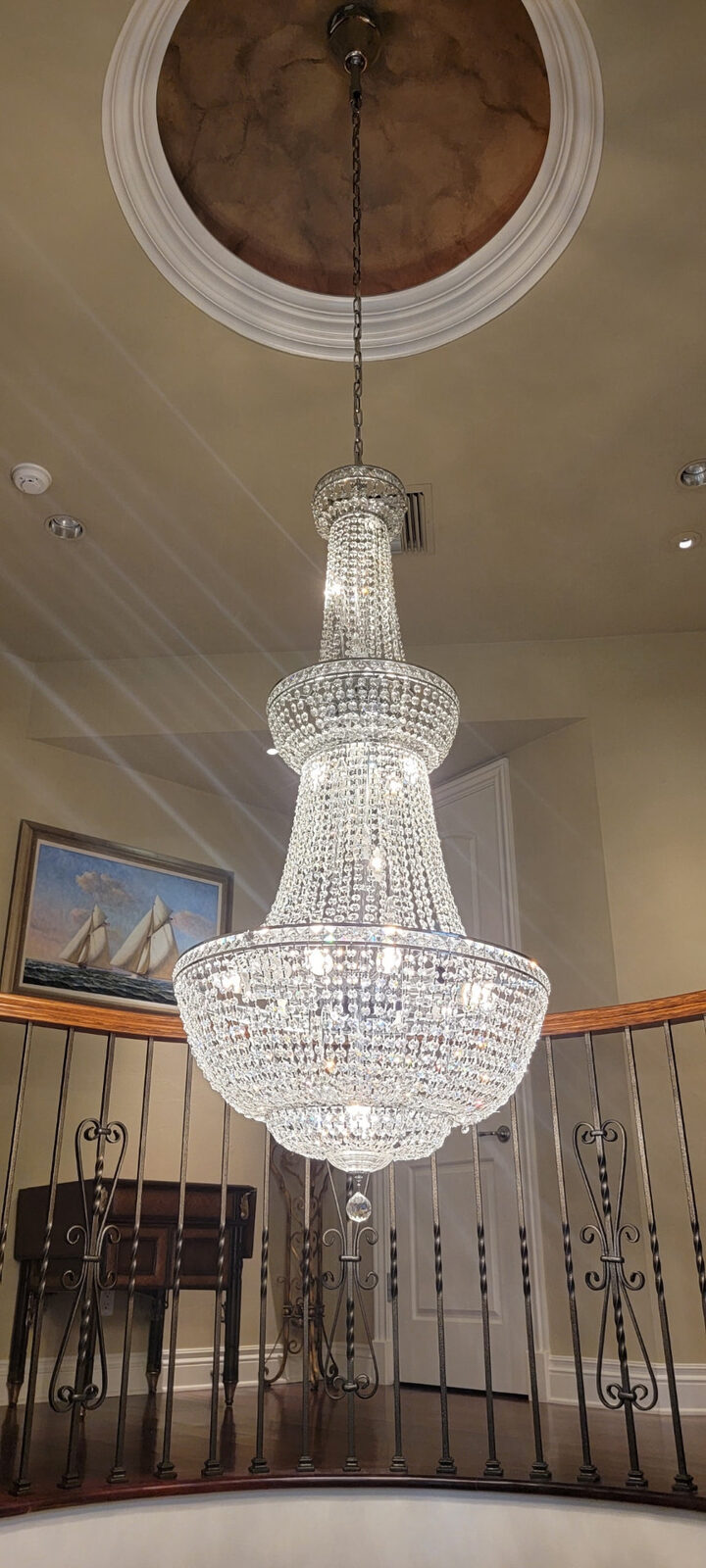 Tiered crystal chandelier hanging in a stairwell above an iron railing