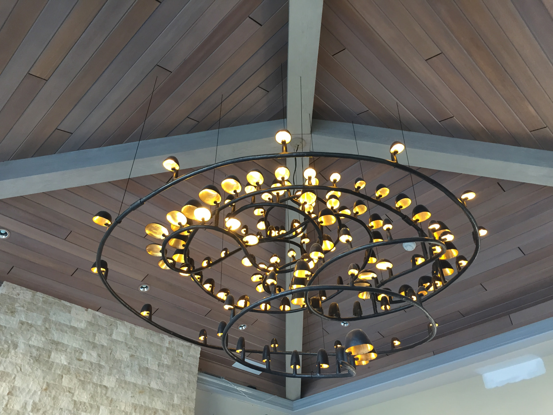Large sculptural iron ring chandelier mounted on a vaulted wood plank ceiling