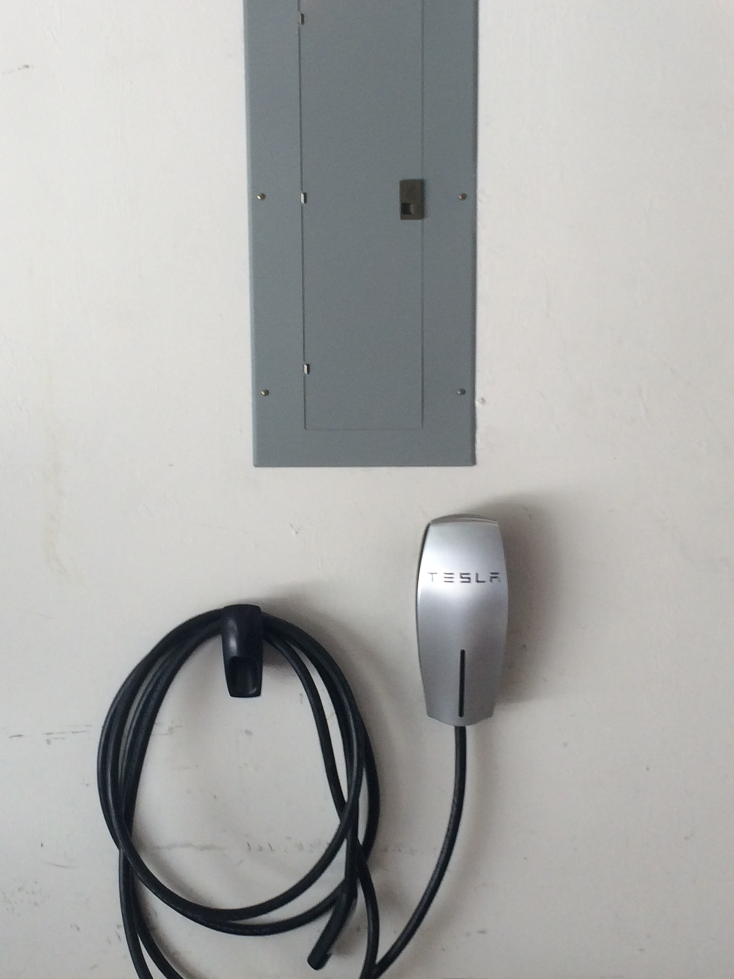Tesla wall connector EV charger installed beside a garage electrical panel
