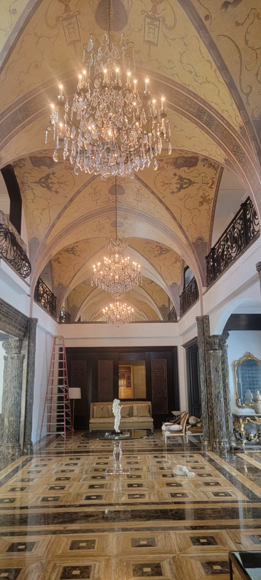 Three crystal chandeliers hung in a row beneath a painted vaulted ceiling in a grand hall
