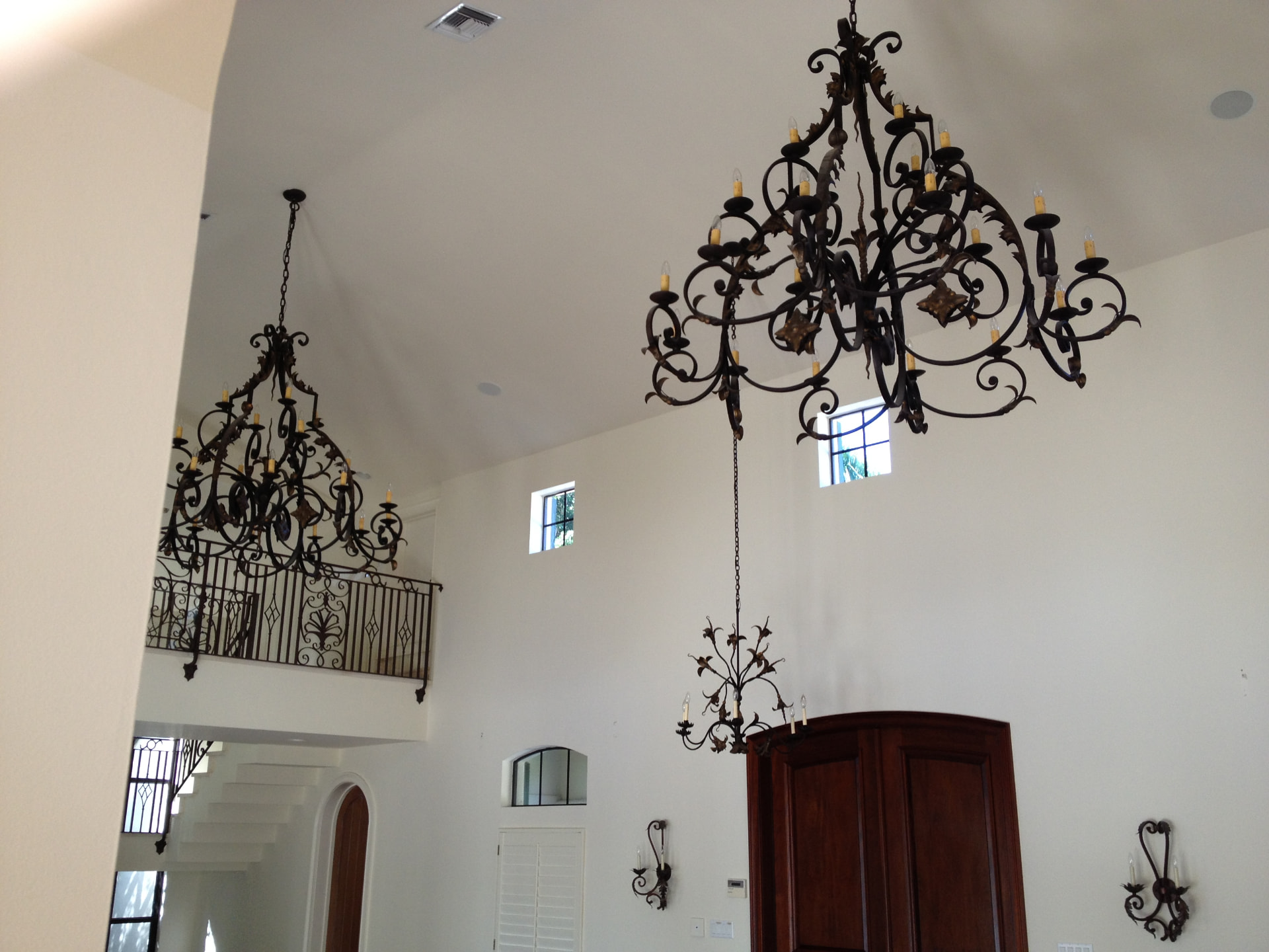 Two wrought iron chandeliers and matching wall sconces in a two-story entry